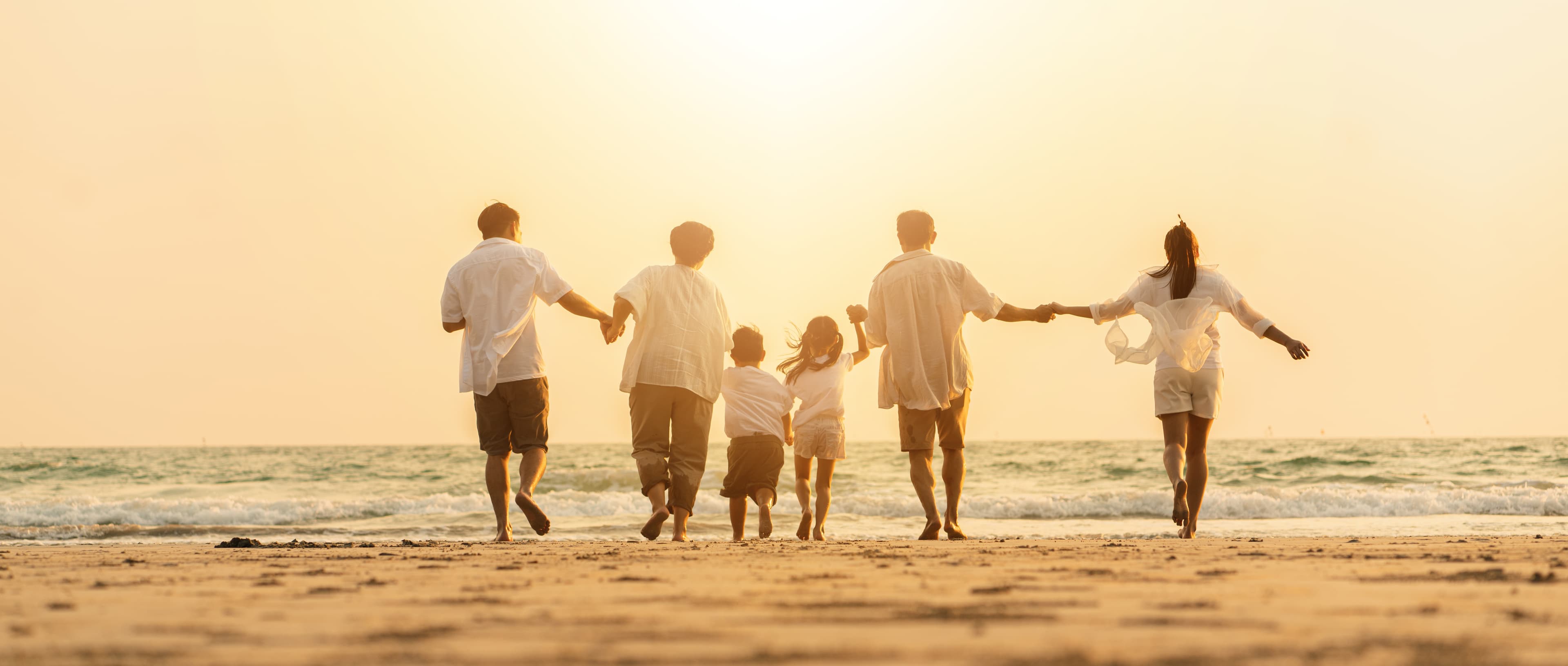 Multi-generational family holding hands walking on a beach at sunset
