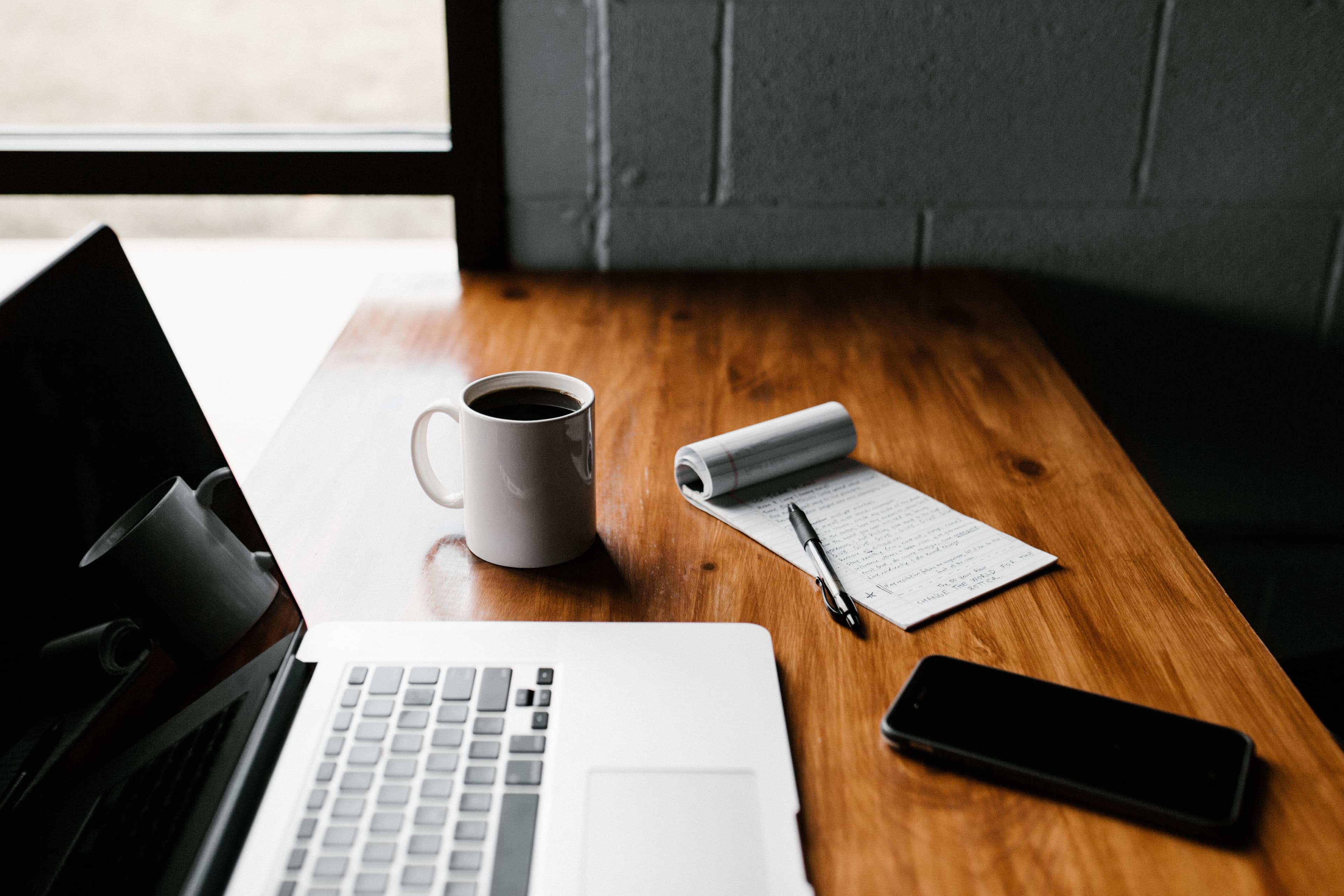 Laptop, notepad, coffee and phone on a well-organised desk